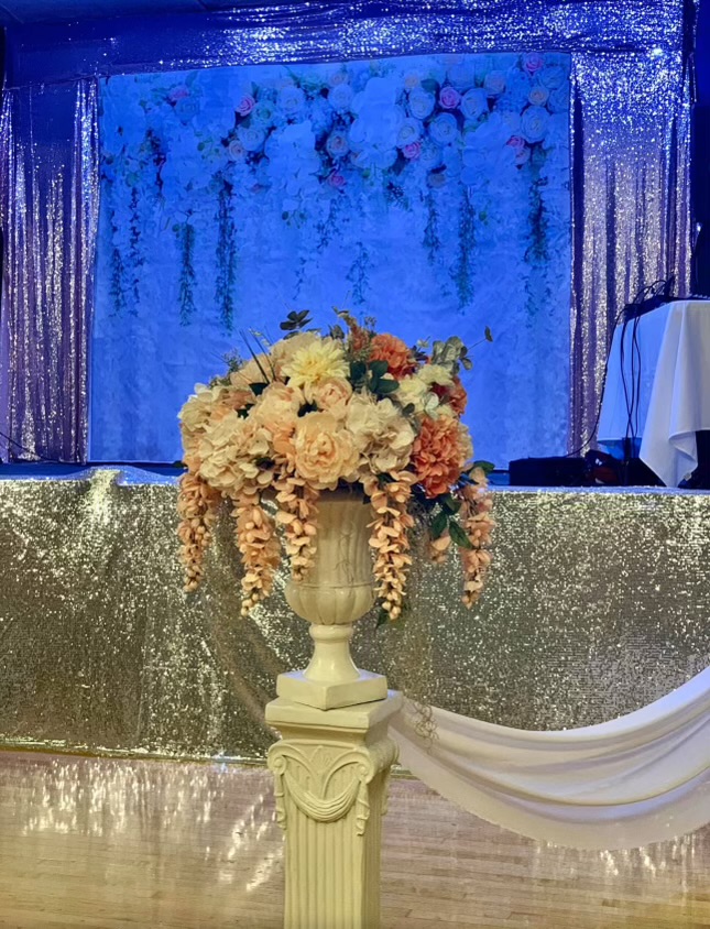 Floral pedestal arrangement in front of blue glitter stage