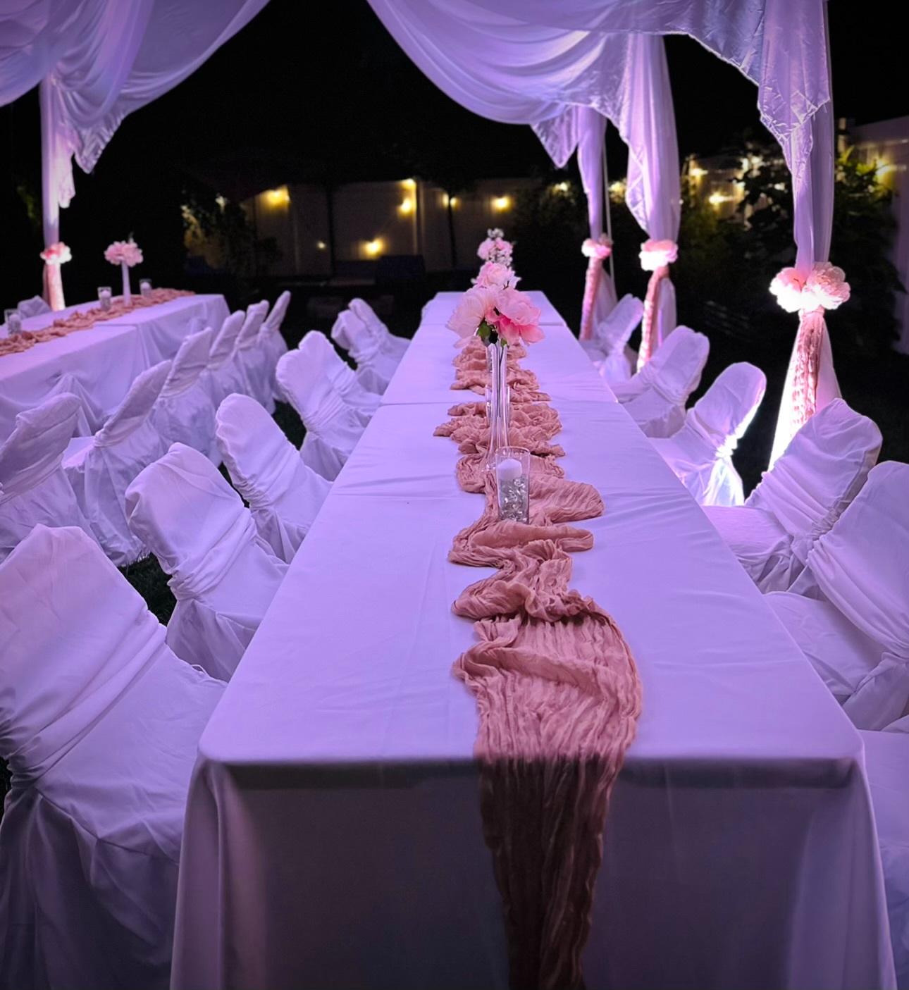 Long banquet table with blush runner under white draping at night